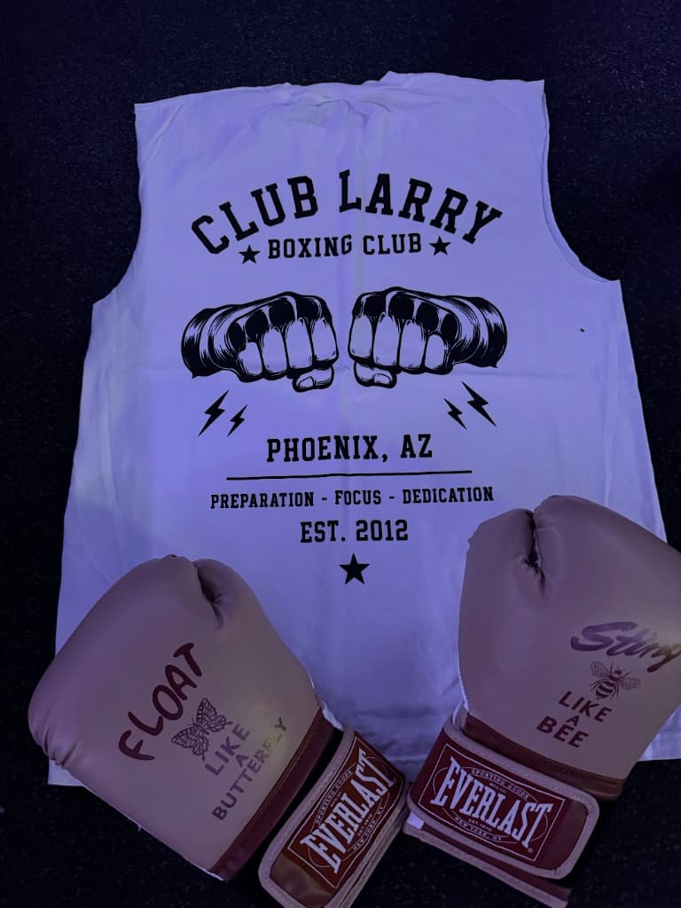 Chalk white Club Larry Boxing Club tank with a black touching-fists print, laid out with rose Everlast gloves